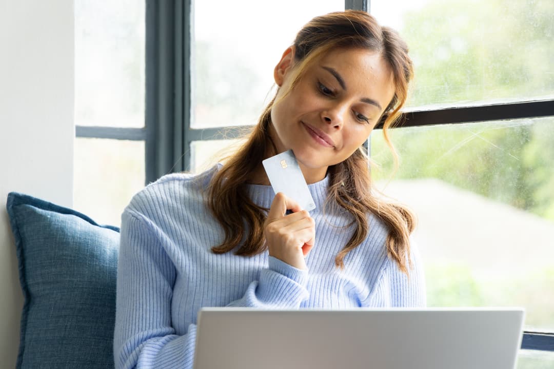 Smiling woman shopping online with credit card at home near window
