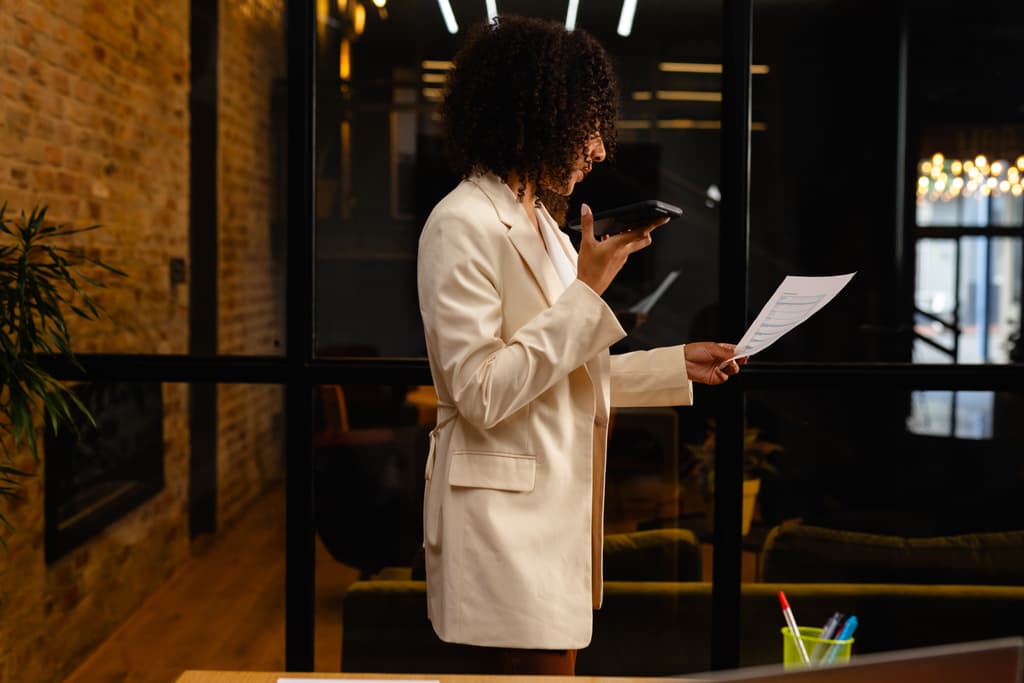 An african american woman is reading a document while using her cellphone in her hotel lobby area
