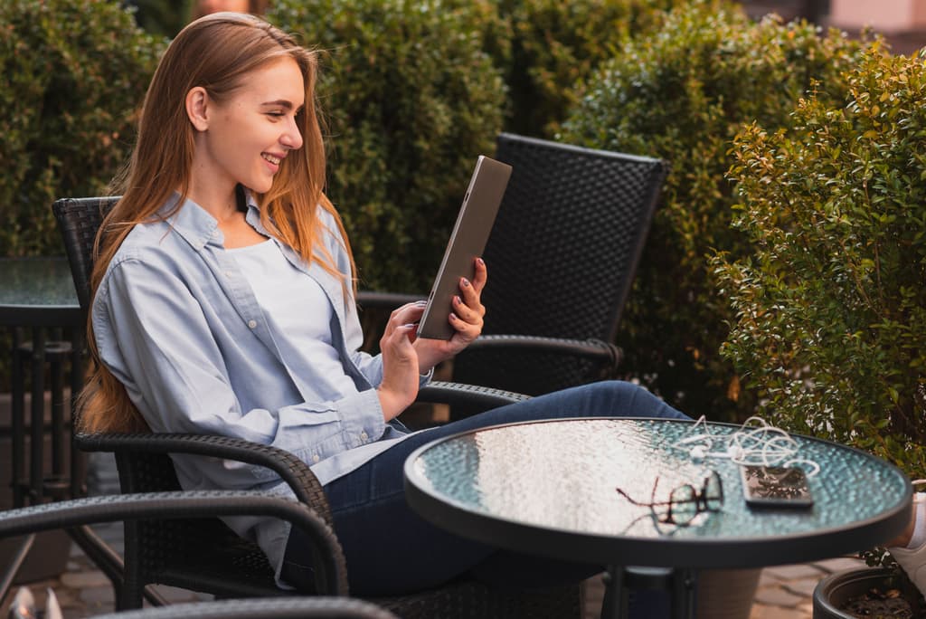 A hotel front desk manager checks her property performance in a tablet while sitting in an outdoor table in her property