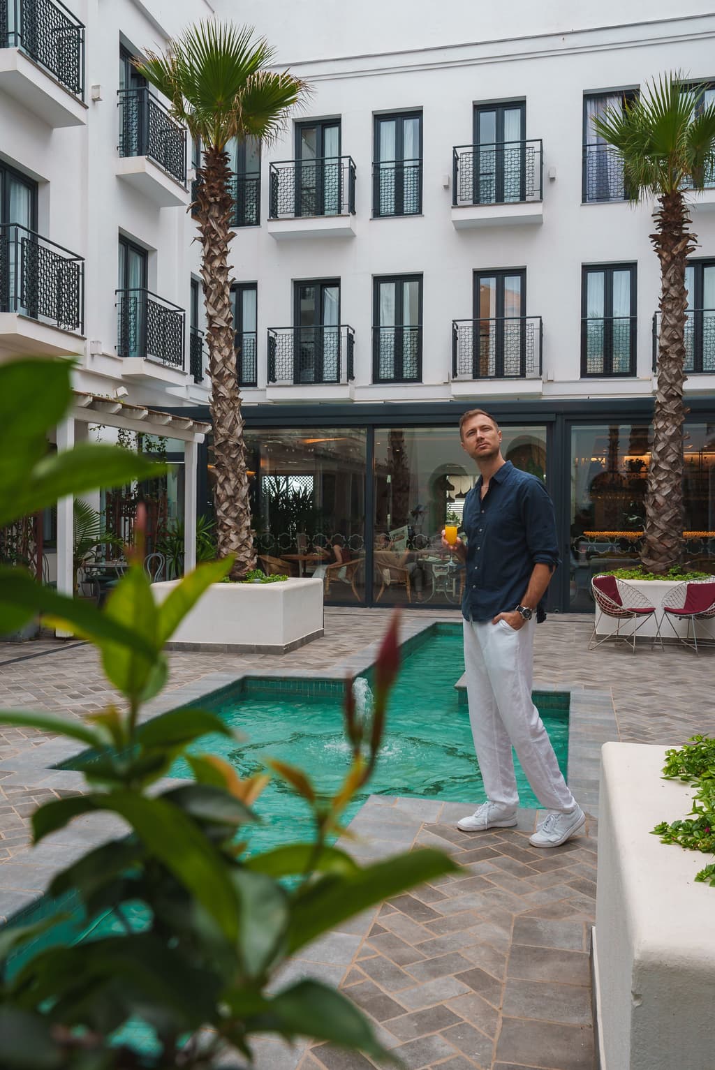 A gentleman stands in a small pool area in the patio of a property with a drink in his hand