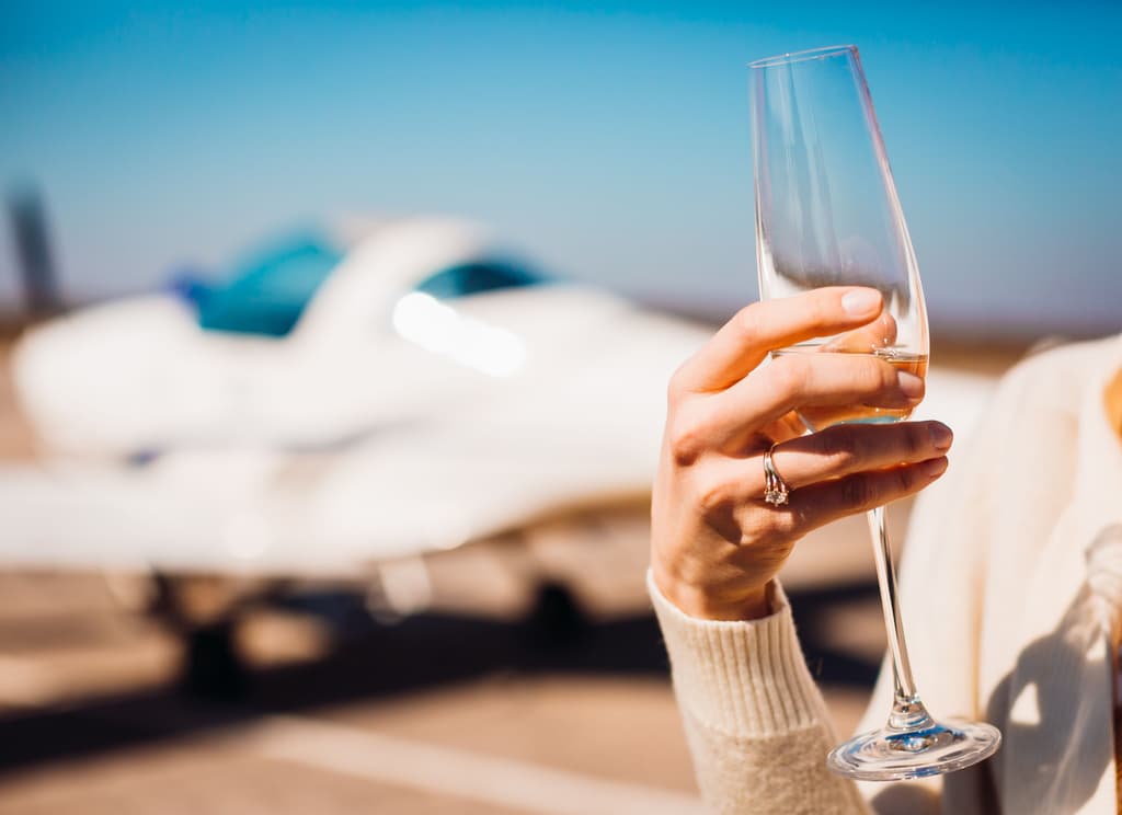 A woman holds in her right hand a champagne glass with a private jet in the background